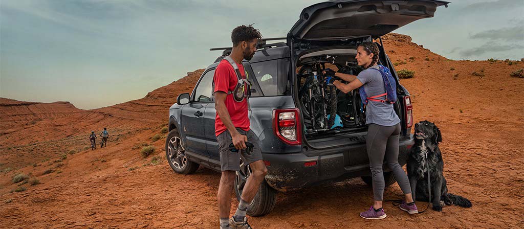 2026 Ford Bronco Sport® parked in the desert with two people standing outside of the vehicle, wearing hiking gear with their dog