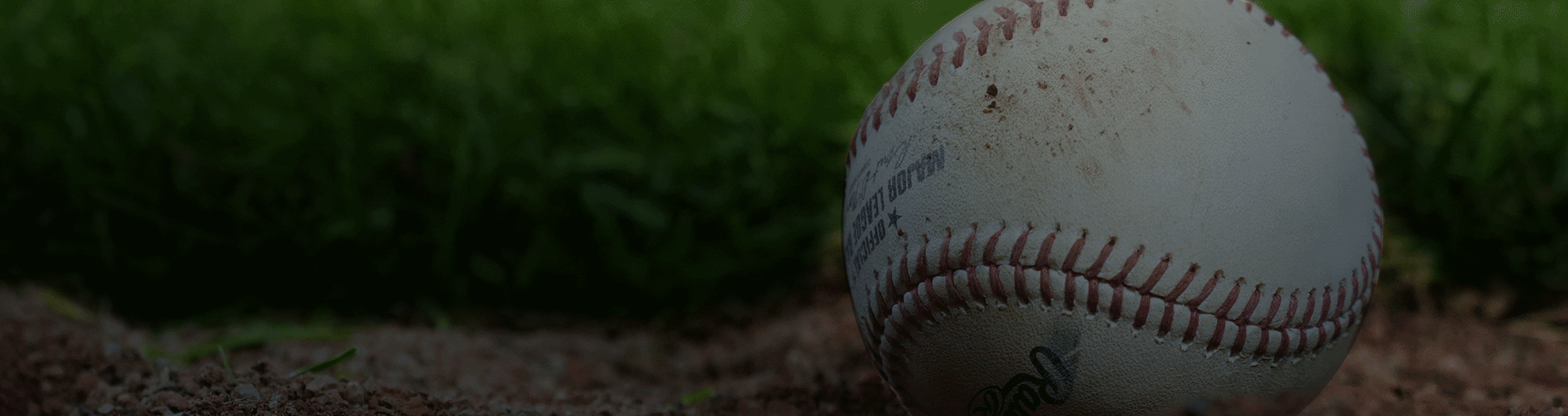 A dirty baseball resting on green grass and brown dirt
