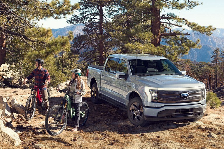 A 2022 Ford F-150® LightningTM parked on rocks in a scenic location with two people on bikes
