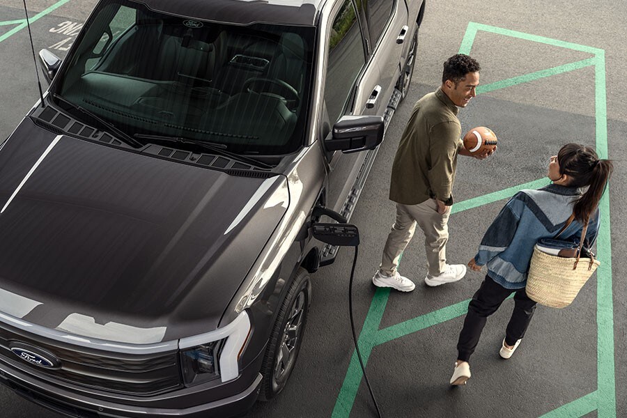 Two people next to a 2022 F-150® LightingTM being charged at a charging station