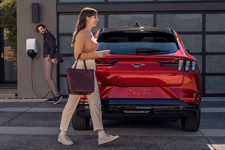 A 2022 Ford Mustang Mach-E® being charged in a driveway in front of a house with two people
