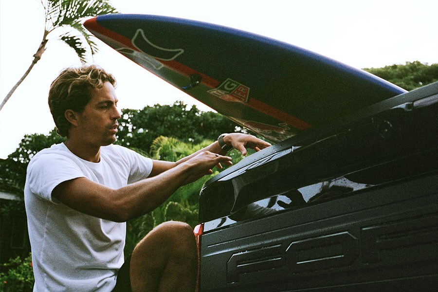 Kai Lenny sujetando su tabla de surf en la plataforma de una camioneta Ford Super Duty®