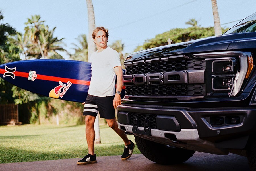 Kai Lenny sosteniendo una tabla de surf camina cerca de una camioneta Ford Super Duty® 2023