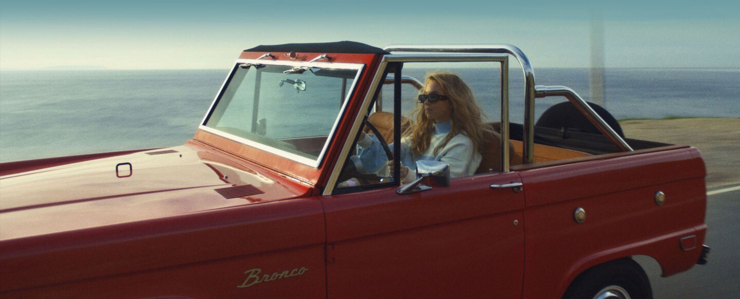 Sydney Sweeney manejando su SUV clásica Bronco® por una carretera junto al océano