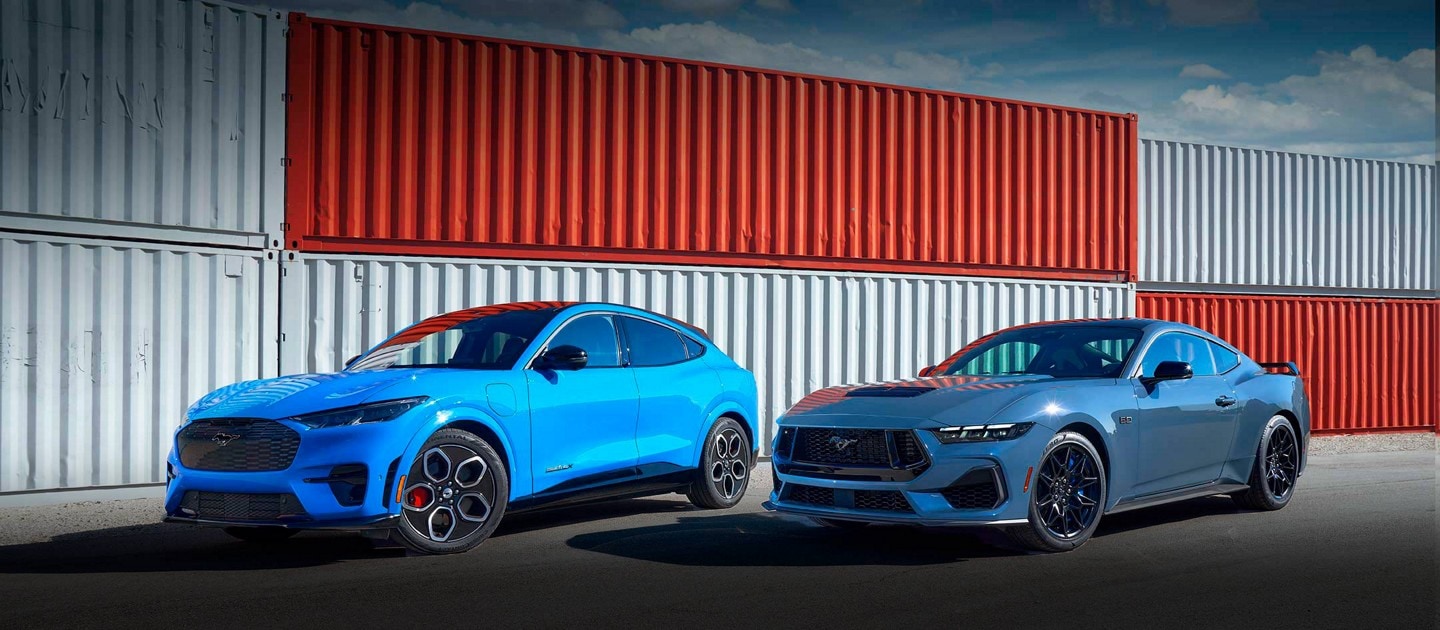 A 2024 Ford Mustang® Mach-E® SUV and a 2024 Ford Mustang® coupe parked near shipping containers