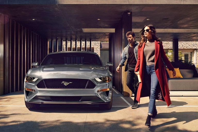 Two people walking away from a 2023 Ford Mustang® coupe parked in a carport