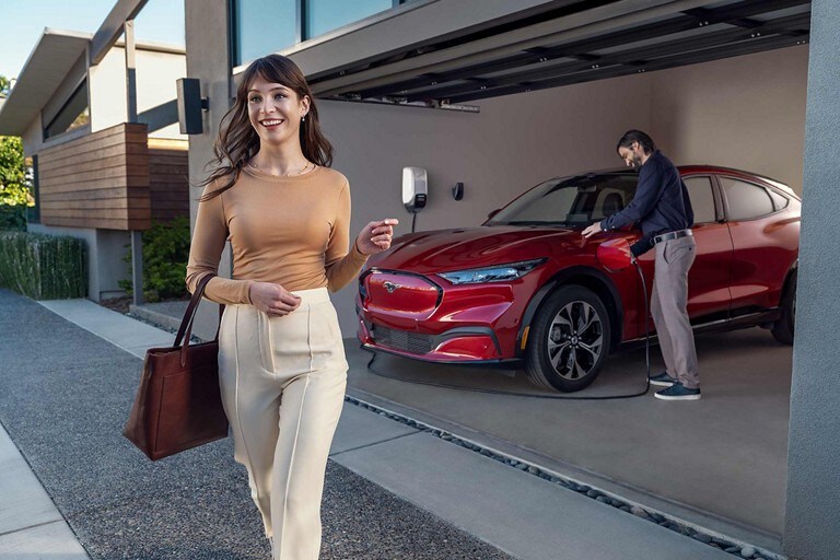 One person walking away from a 2023 Ford Mustang® Mach-E® SUV as another plugs in the charger in a garage