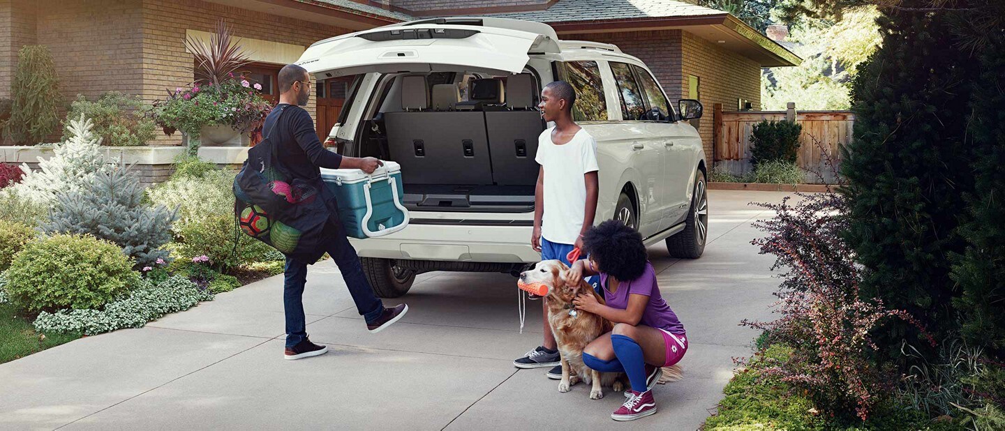A family loading sports gear into the rear cargo area of a Ford Expedition