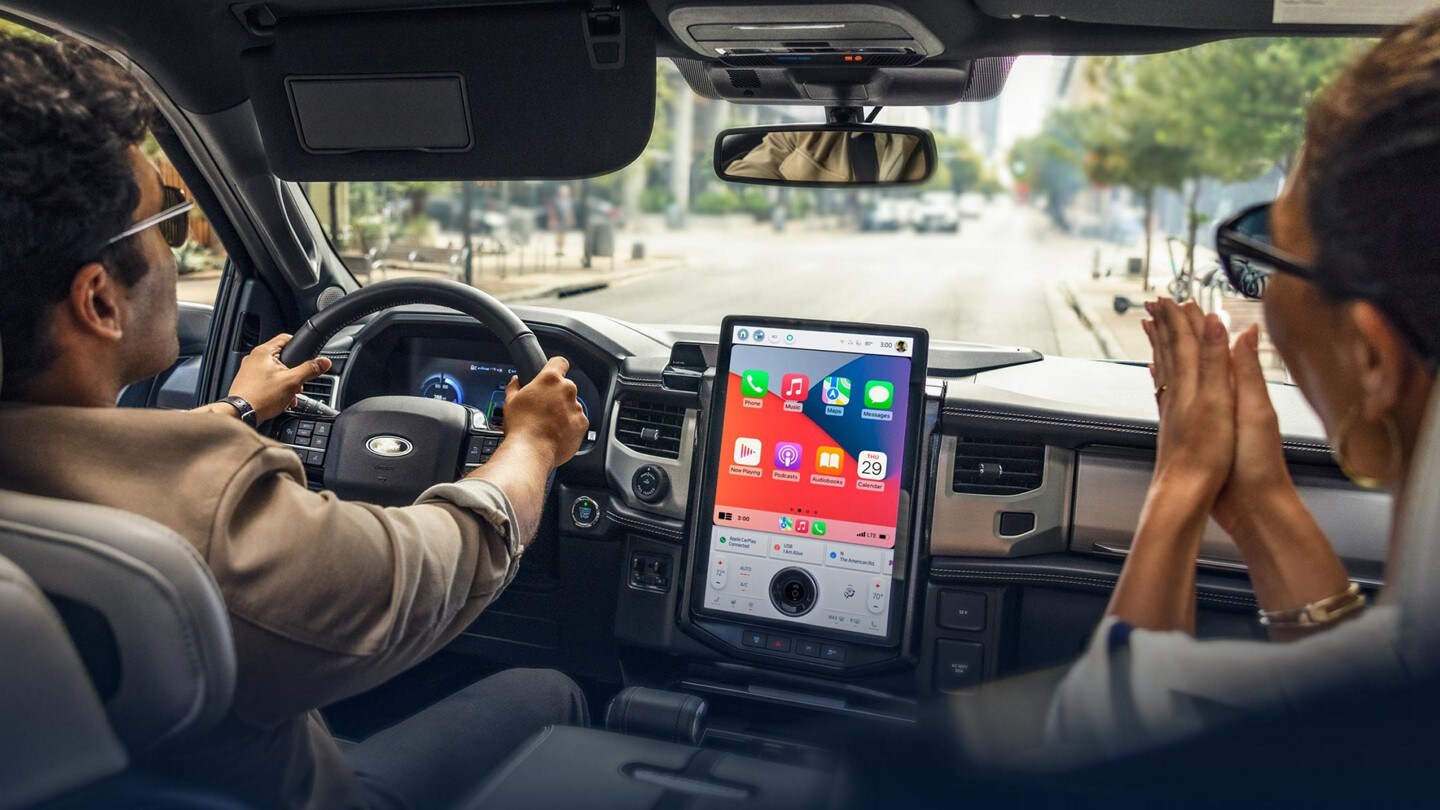A driver and passenger traveling in a 2023 Ford F-150® Lightning®. A SYNC® 4A display showing Apple apps is prominent