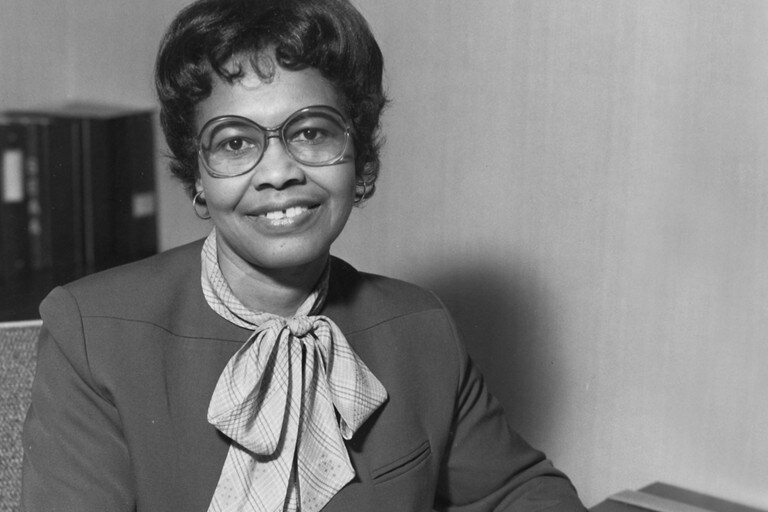 Vemos una foto en blanco y negro de la innovadora automotriz, la Dr. Gladys West en su escritorio.