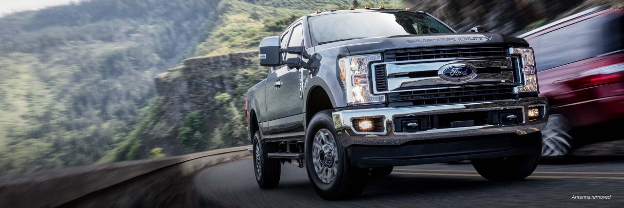 Three-quarter perspective of the front end of a Ford [Insert model] truck being driven on a curved scenic highway