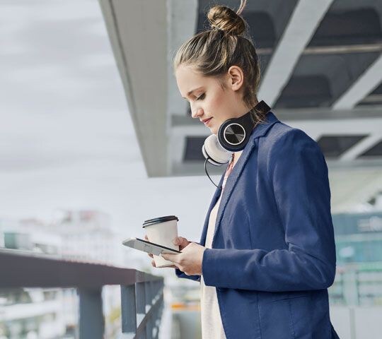 Woman with headphones holding coffee and using FordPass on phone