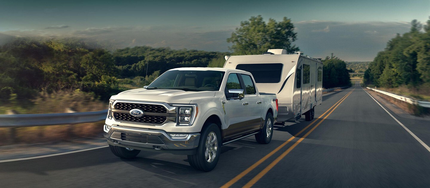 A 2021 Ford F One Fifty towing a camper on a two lane highway