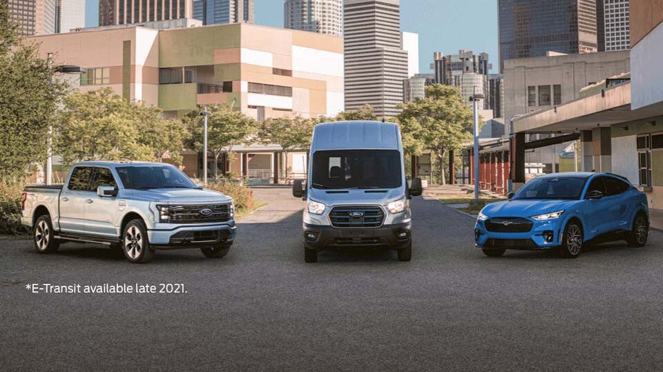2022 Ford Mustang Mach-E 2022 Ford F-150 Lightning and 2022 Ford E-Transit parked in front of a large city