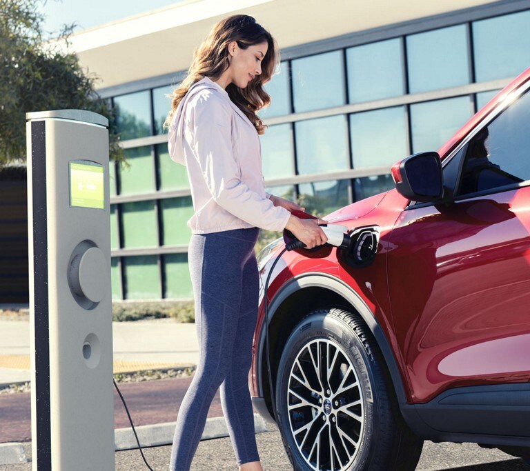View of a woman plugging a charger into a parked Ford Escape Plug In Hybrid