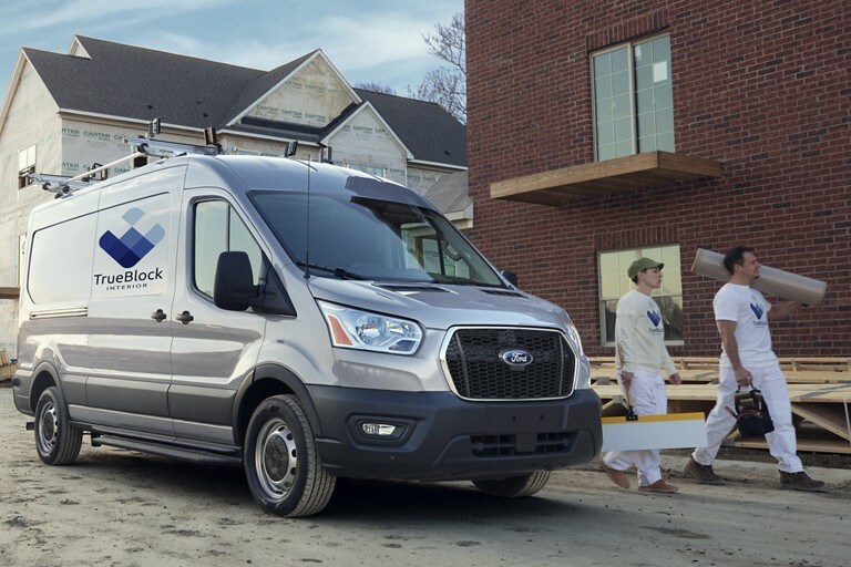 A 2022 Ford Transit parked at a job site with two workers walking away from it