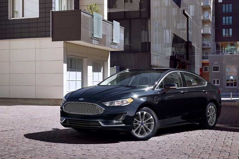 Un Fusion Plug in Hybrid Titanium 2020 en Agate Black estacionado en frente de un moderno complejo de departamentos