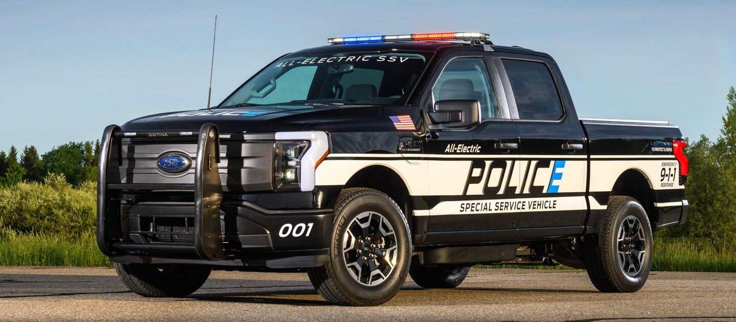 Side view of one 2023 Ford F-150®️ Lightning™️ Pro SSV truck parked with background of trees and bushes