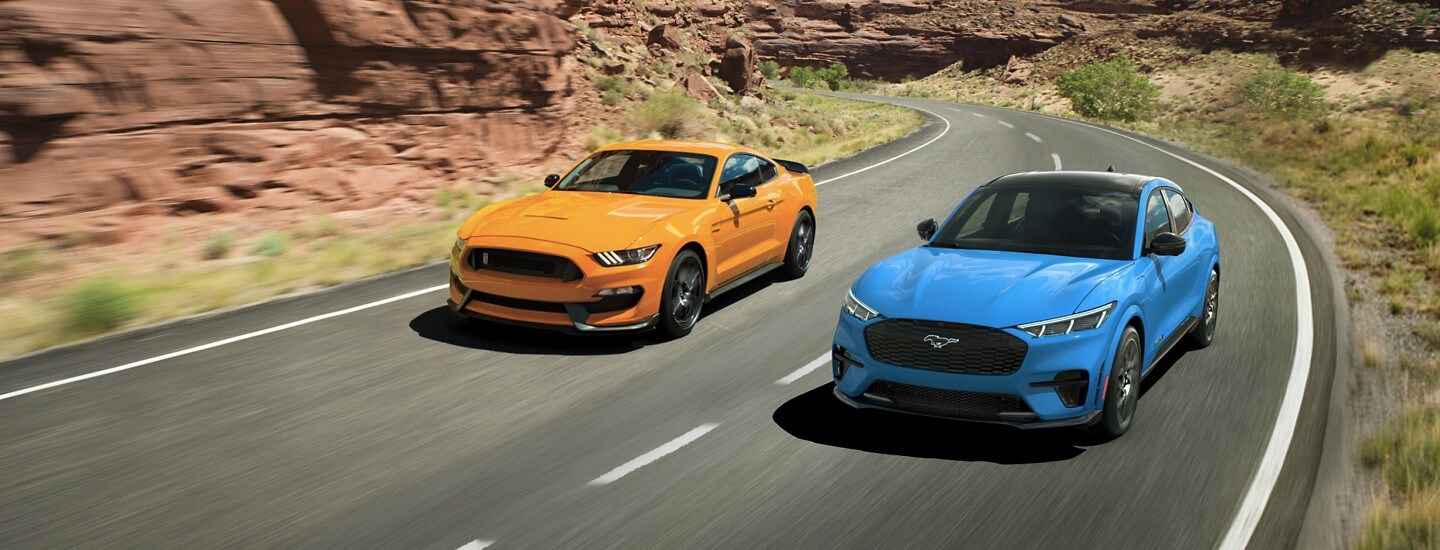 Two Ford Mustangs drive around a curve on a paved road.