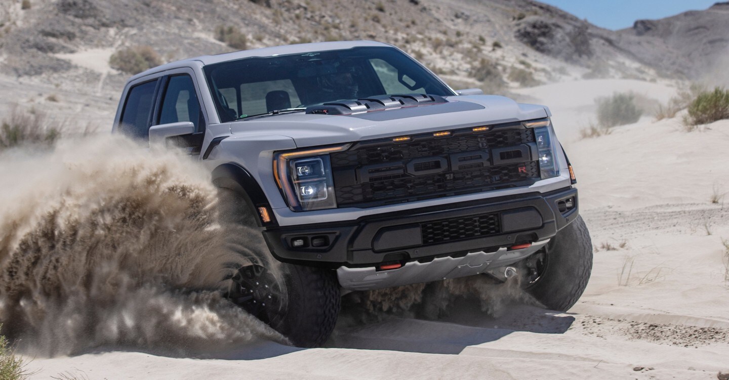 A Ford F-150 Raptor R drives over sandy, uneven terrain.