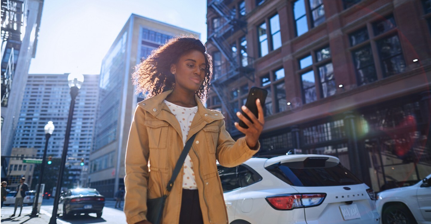 A woman is looking down at a smartphone she’s holding