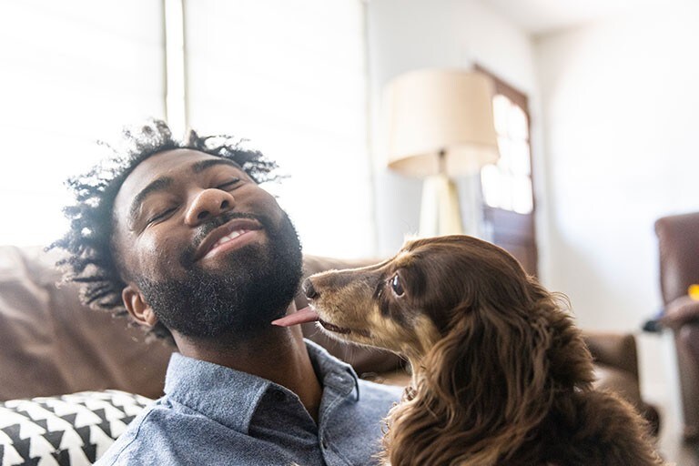 A man smiling while his dog playfully licks his chin.