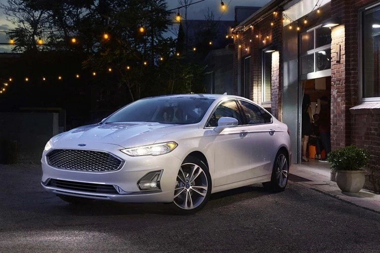 White 2020 Ford® Fusion shown parked in front of a brick building with patio lights strung up above it