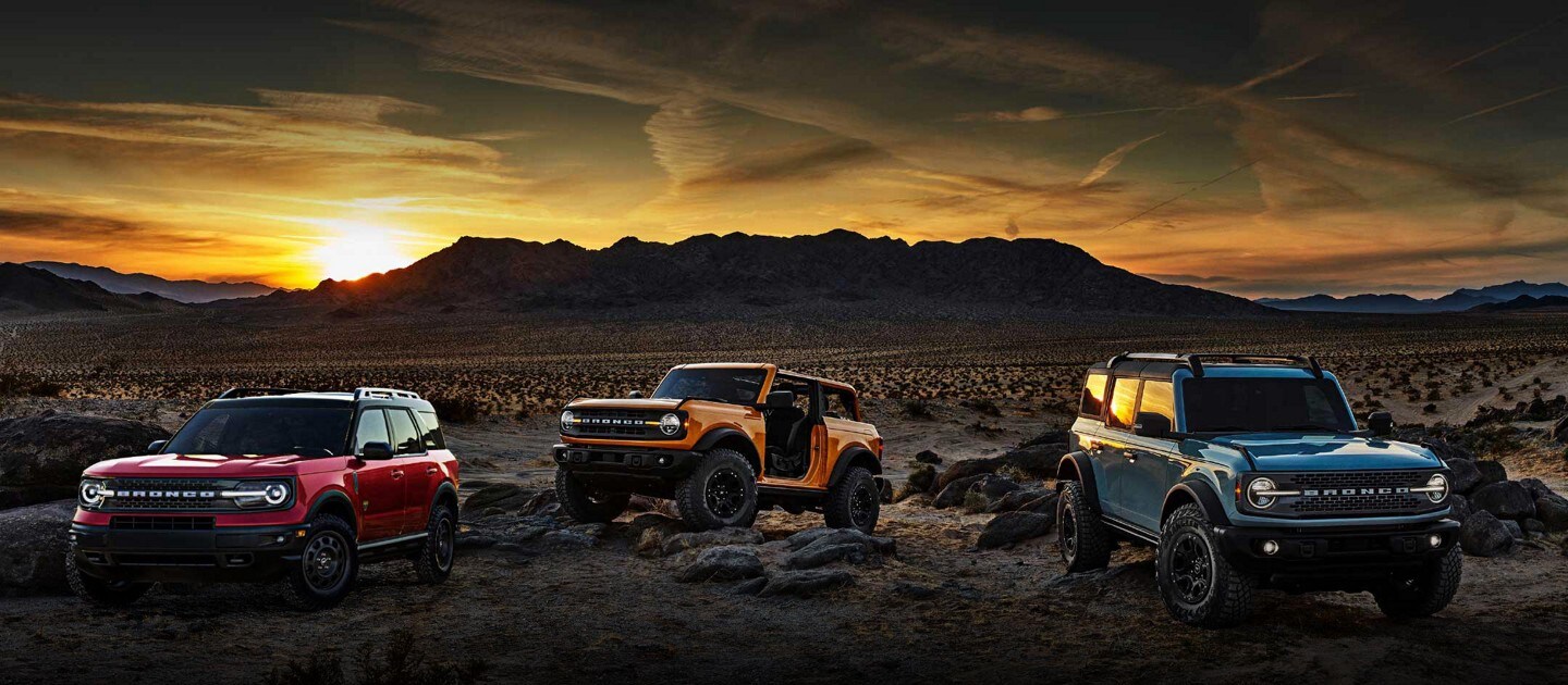 Dos SUV Ford Bronco® 2022 y una SUV Bronco® Sport estacionadas en la cima de una montaña al atardecer