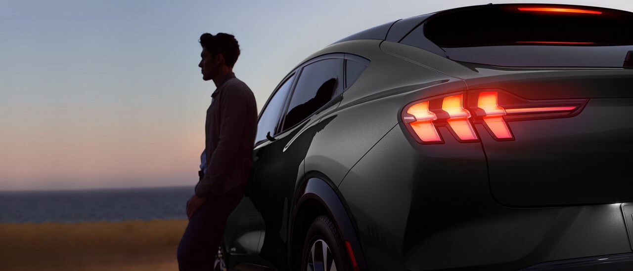 Hombre apoyado sobre el costado de una Ford Mustang Mach-E® 2023 al anochecer