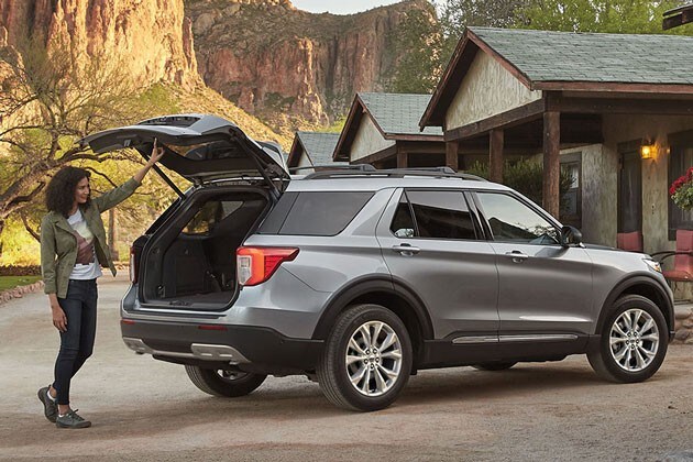 2023 Ford Explorer shown in profile with the rear liftgate open with a woman standing behind it.