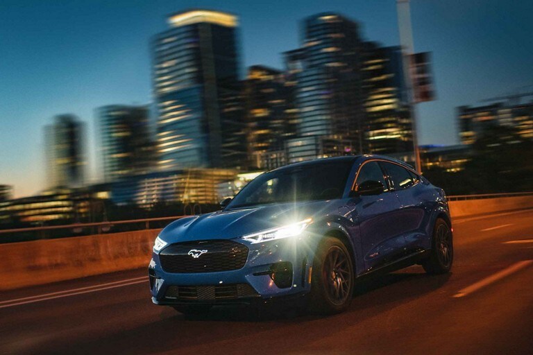 Vista exterior de una Mustang® Mach-E® 2023 andando al anochecer en una carretera