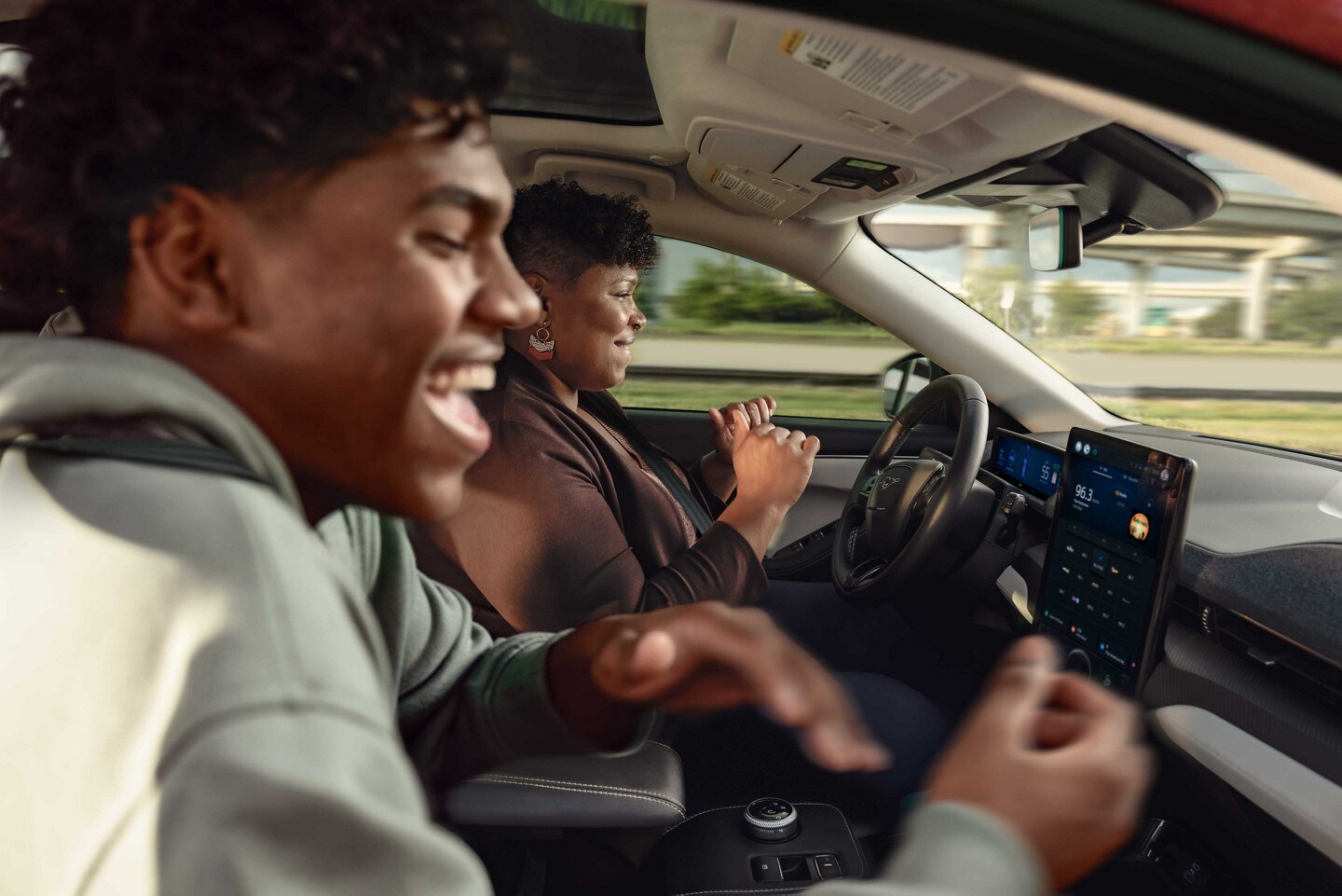 Una madre y su hijo sonriendo en una Mustang Mach-E mientras usan BlueCruise en la carretera. 