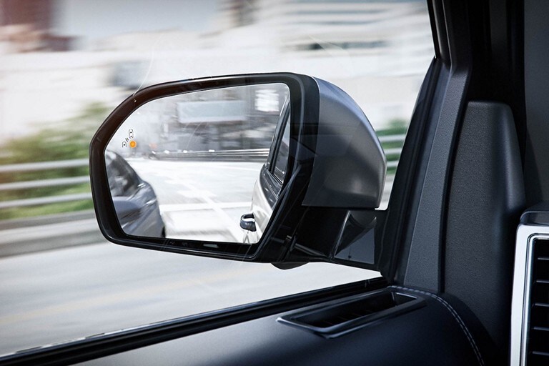 Driver side rearview mirror with indicator light showing vehicle detected in blind spot