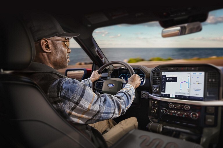 Una persona al volante conduciendo una Ford F-150 2022 con el océano de fondo
