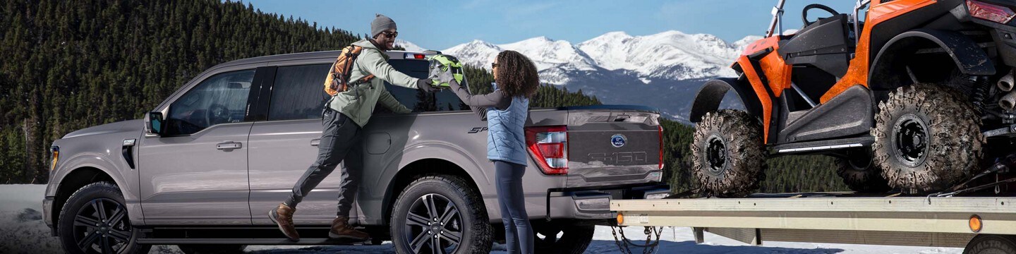 Una pareja descargando equipos de la plataforma de una Ford F-150® LARIAT 2022 enganchada a un remolque con un vehículo todo terreno