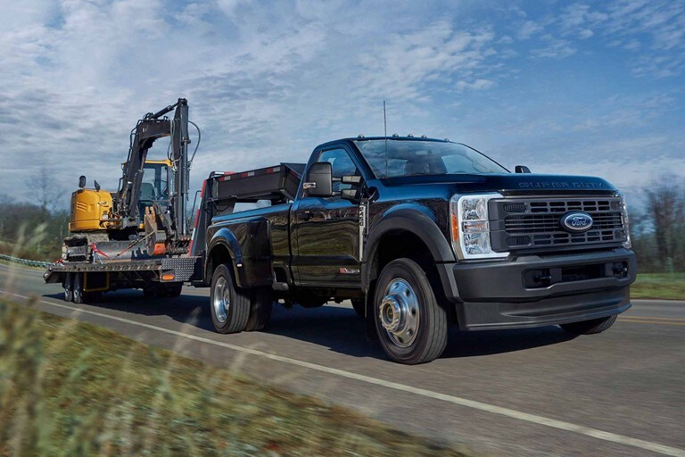 2023 Ford F-450 Super Duty trailering a large tractor down a highway
