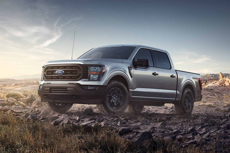 A 2023 Ford F-150 being driven in a boulder-strewn off-road trail kicking up dust