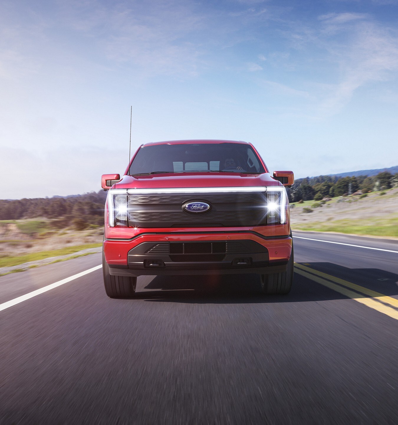 Head-on shot of a Rapid-Red 2022 F-150 Lightning driving down the highway.