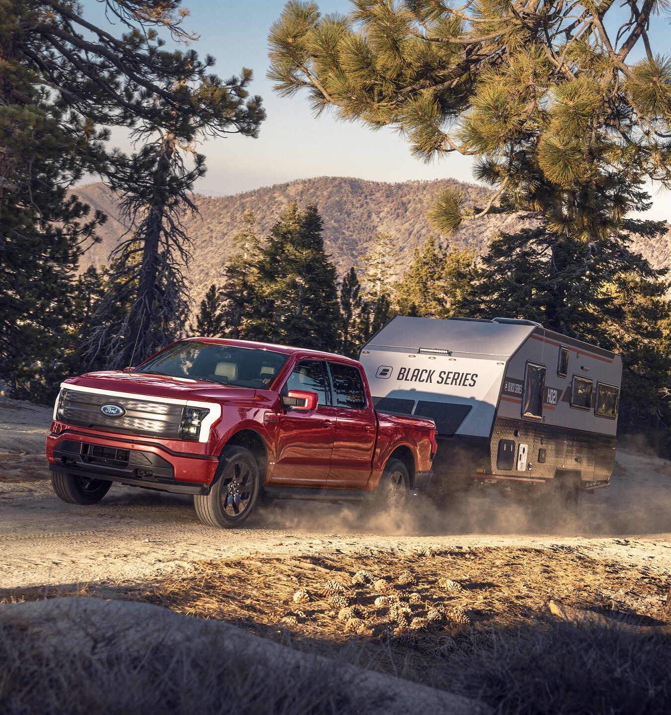 Rapid-Red 2022 F-150 Lightning towing a camper on a forest dirt road.