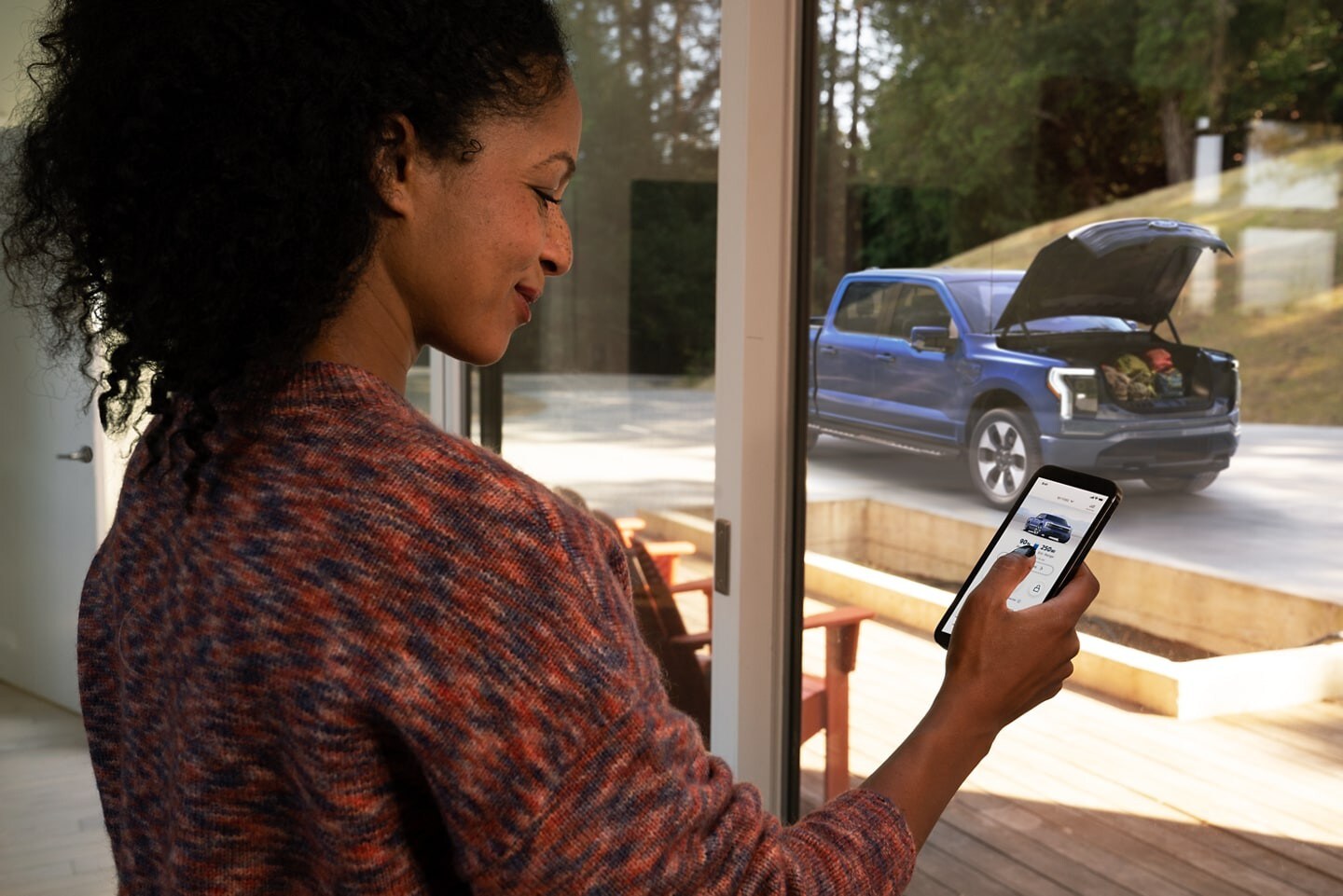 Woman opening the Mega Power Frunk of her Atlas Blue 2022 F-150 Lightning using her smartphone from inside the house.