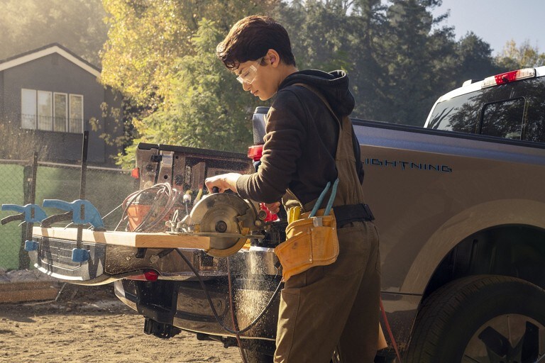 Man saws a wood board clamped to the tailgate of his 2022 F-150 Lightning.
