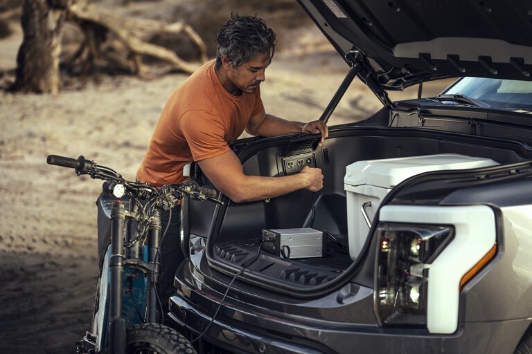 Man plugging a power cord into an outlet in the Mega Power Frunk of his 2022 F-150 Lightning.