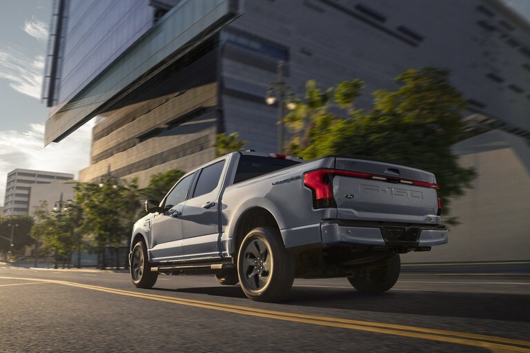 Stone Gray 2022 F-150 Lightning driving down a city street at sunset.