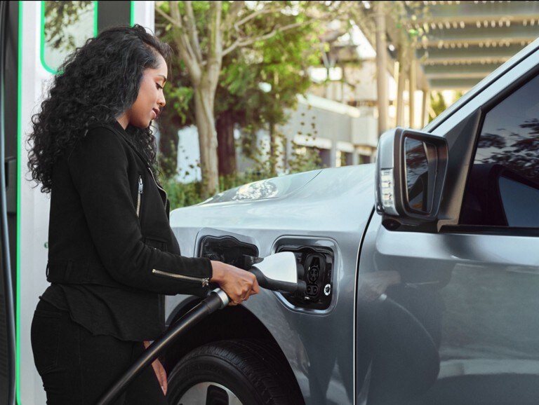 Woman plugging her Iced Blue Silver 2022 F-150 Lightning into a public charging station.