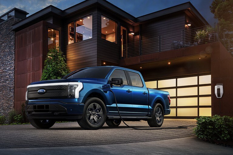 Antimatter Blue 2022 F-150 Lightning plugged into a charger outside of a home at dusk.