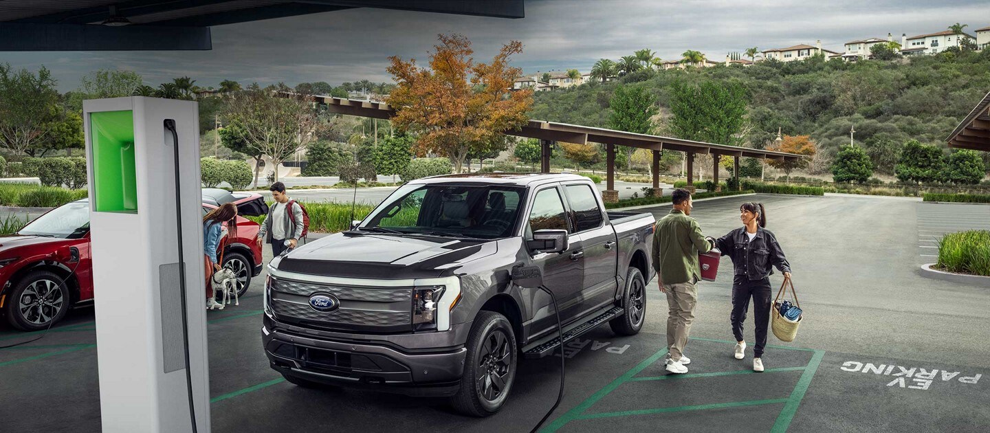 Un hombre y una mujer sentados en la puerta trasera abierta de una Ford F-150® Lightning™ mientras se carga