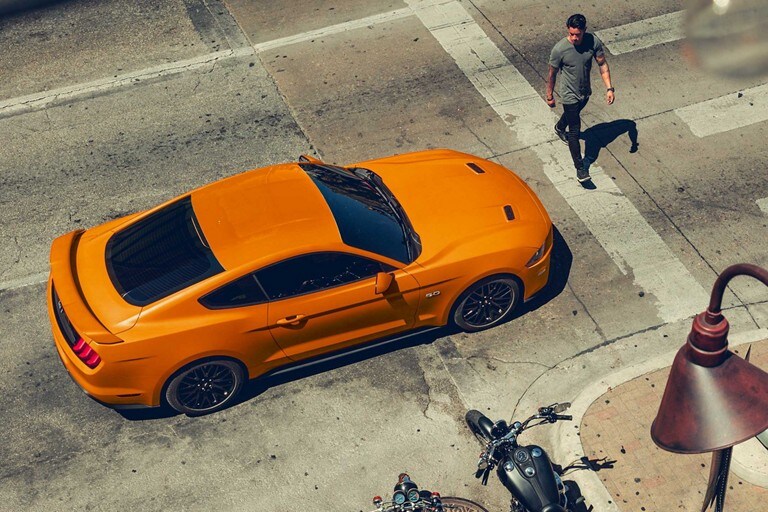 A person walking past a 2020 Ford Mustang in Twister Orange stopped at a crosswalk