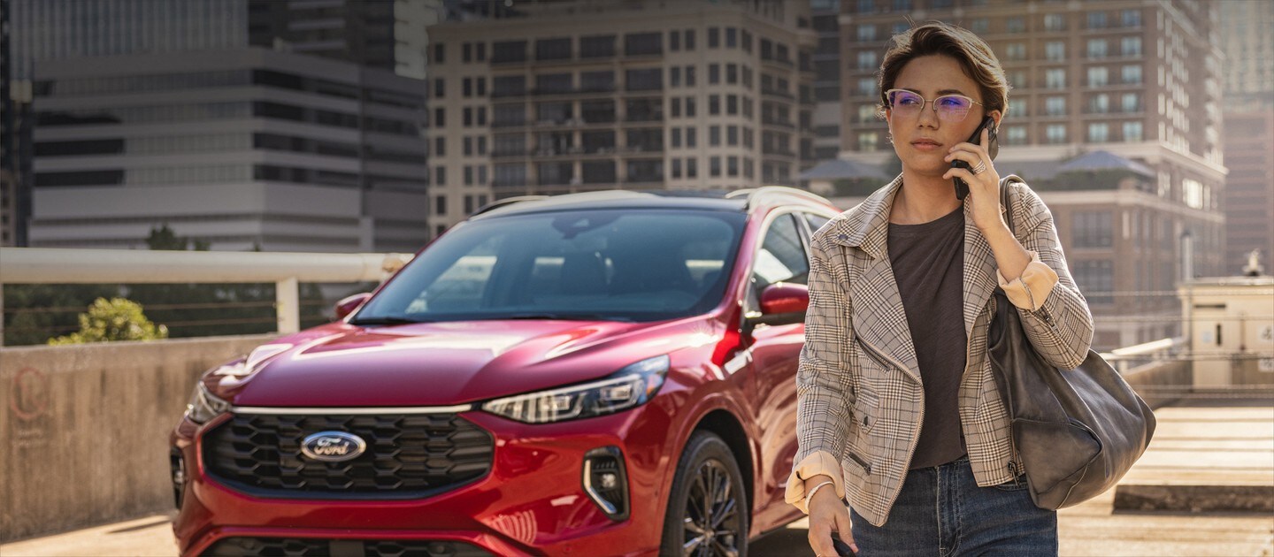 Una mujer hablando por su teléfono móvil y alejándose de una Ford Escape ST-Line Elite 2023