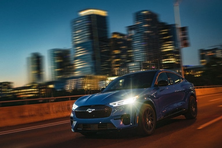 A Mustang Mach-E GT Performance Edition driving at night with a city in the background