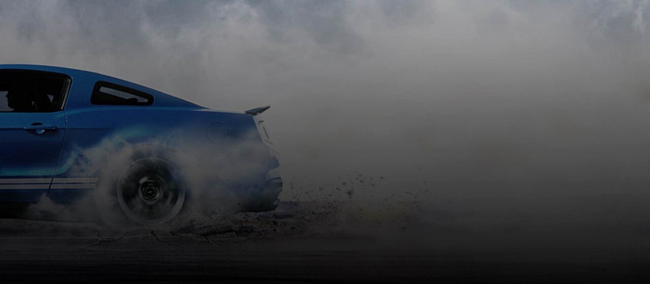 Un Ford Mustang G T 500 2014 en Velocity Blue con Franjas White con ruedas traseras haciendo humo y levantando polvo